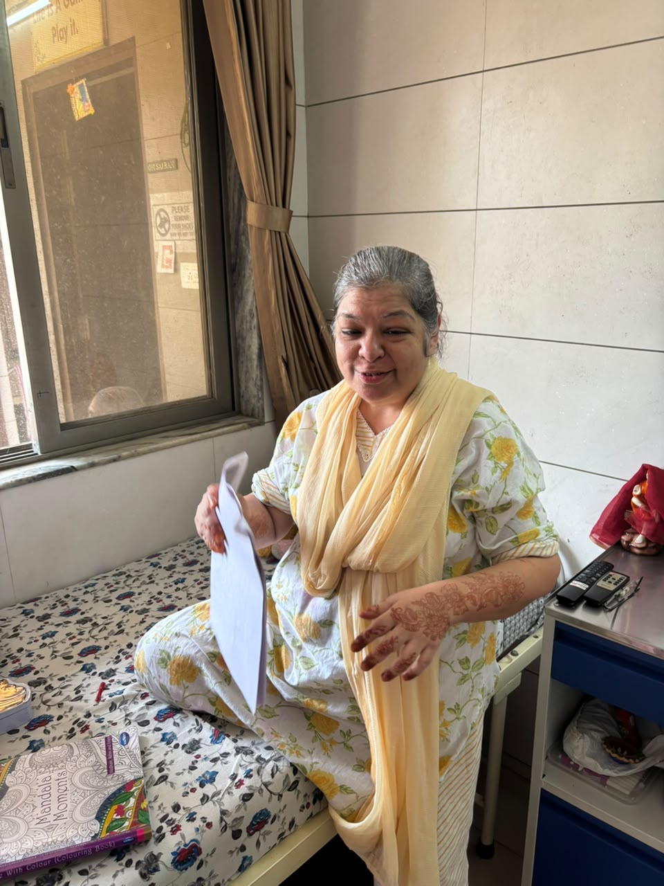 A resident sitting on her bed in her room at the home, looking through the pages of a colouring book
