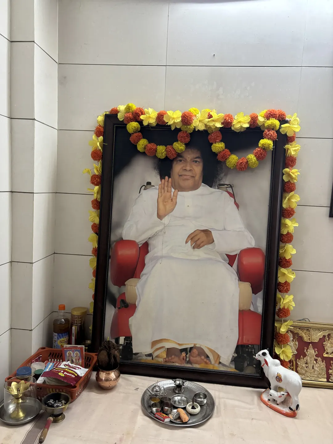 A garlanded framed portrait with flowers, lamps and offerings placed before it at a shrine