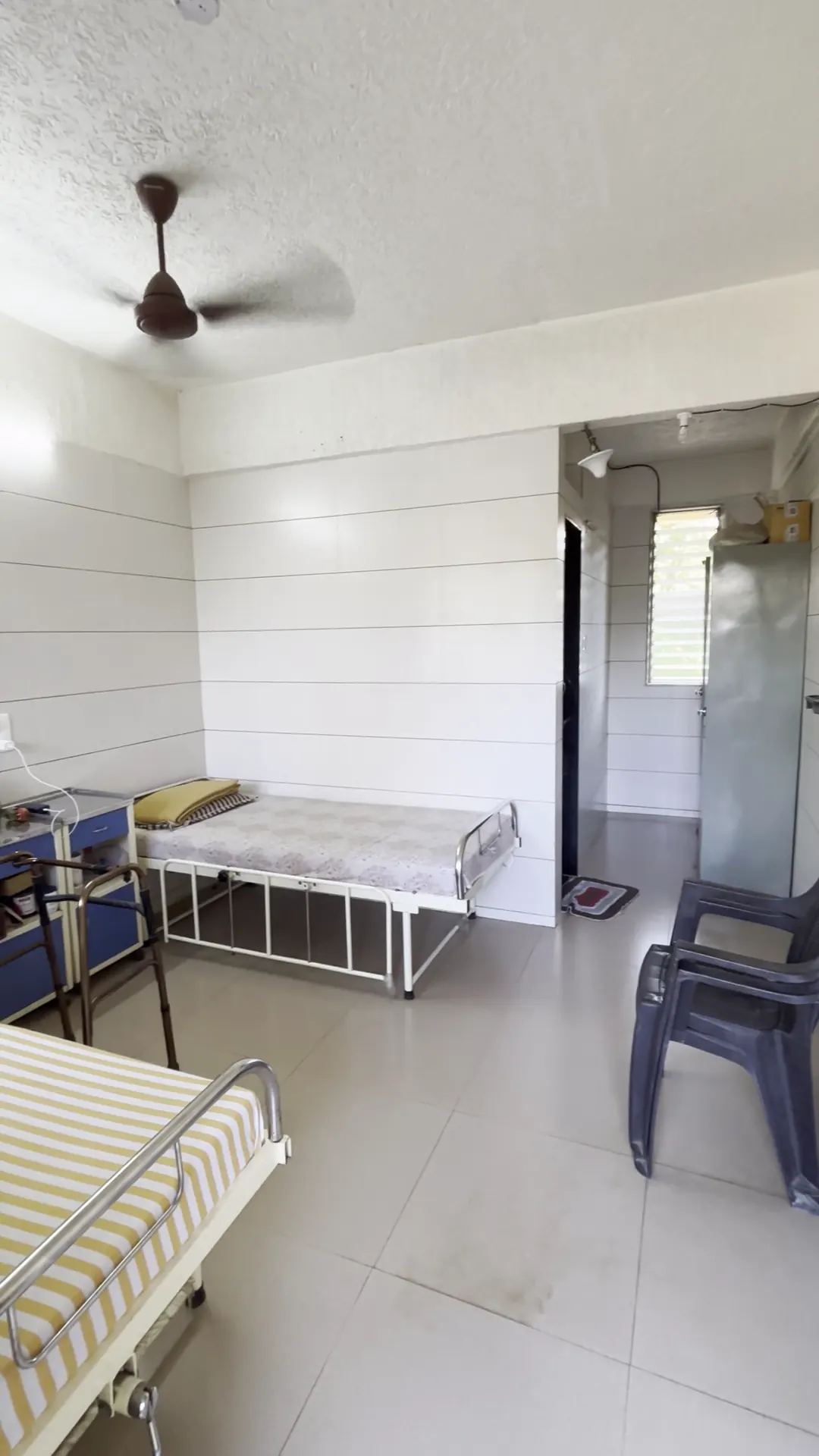 A bright room with two beds, a chair and a ceiling fan